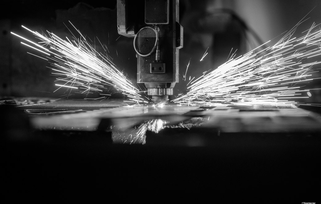A laser cutting head throwing sparks across sheet metal